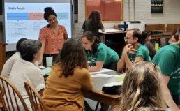 A group of teachers at a table listening to a presenter